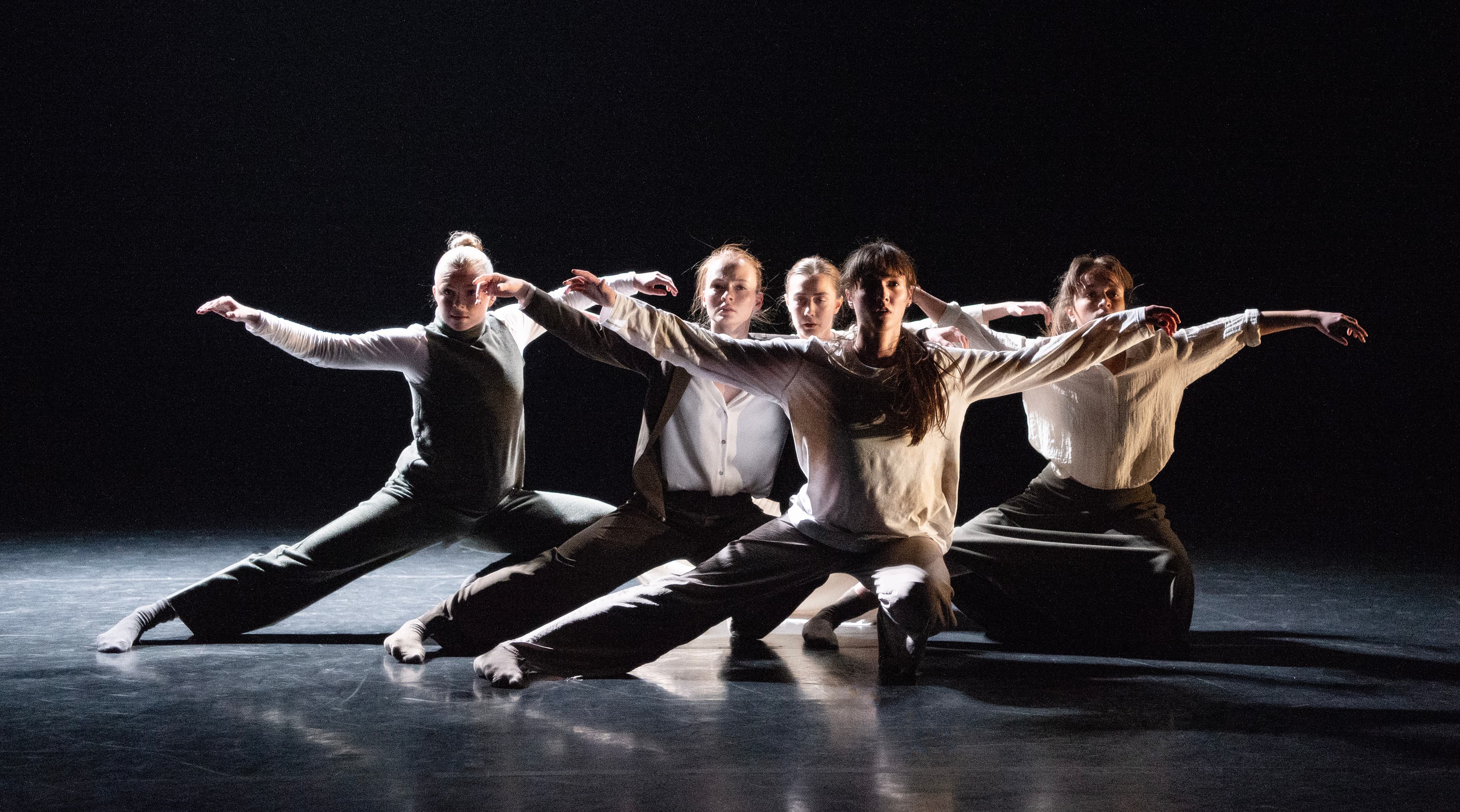 Fem dansere i synkron bevegelse på en scene. Foto